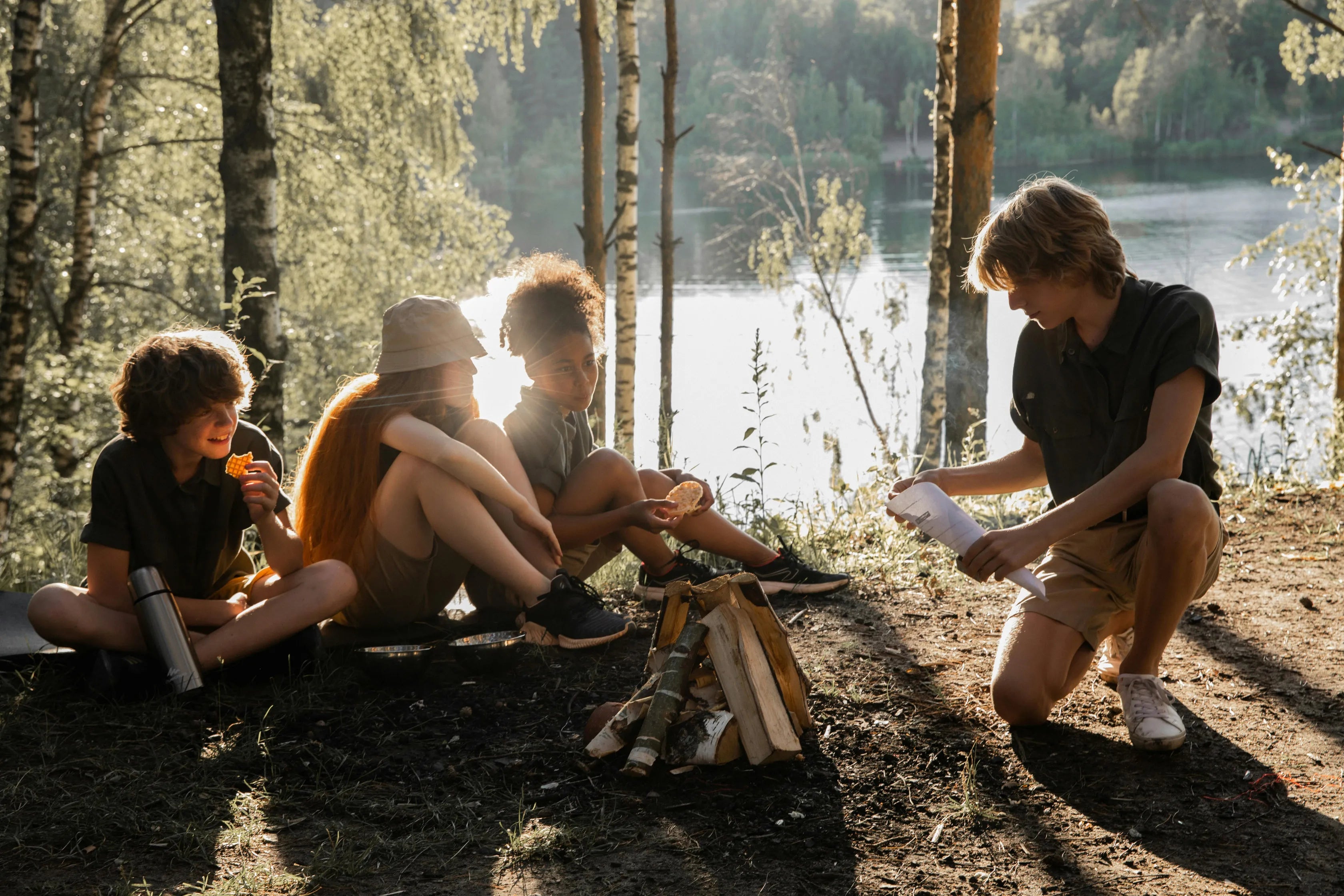 Un groupe d’amis en pleine nature, assis autour d’un feu de camp au bord d’un lac, profitant d’une micro-aventure sportive le temps d’un week-end.